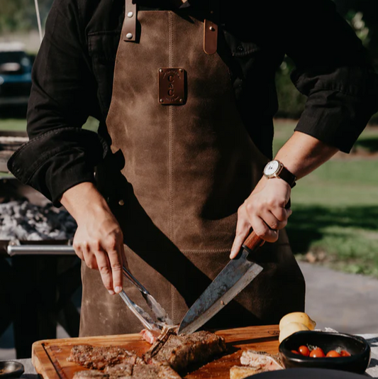 Chef wearing dark brown buff leather apron with adjustable waist belt and neck strap, flame and spark resistant, durable workshop and grilling apron